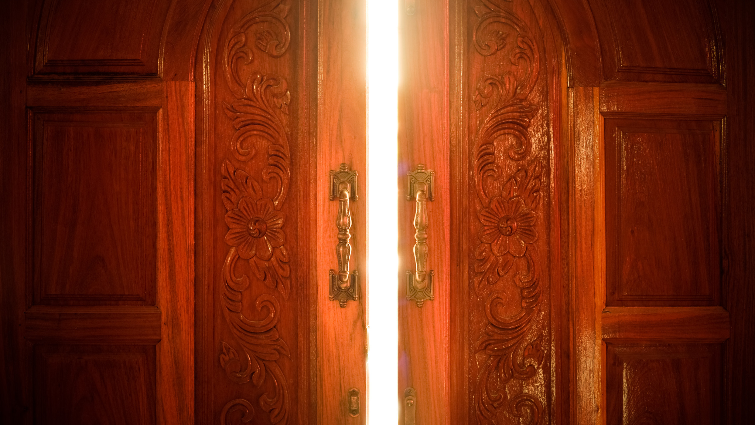 Två äldre trädörrar i en port som öppnad lite, bakom ser man ett starkt ljus.