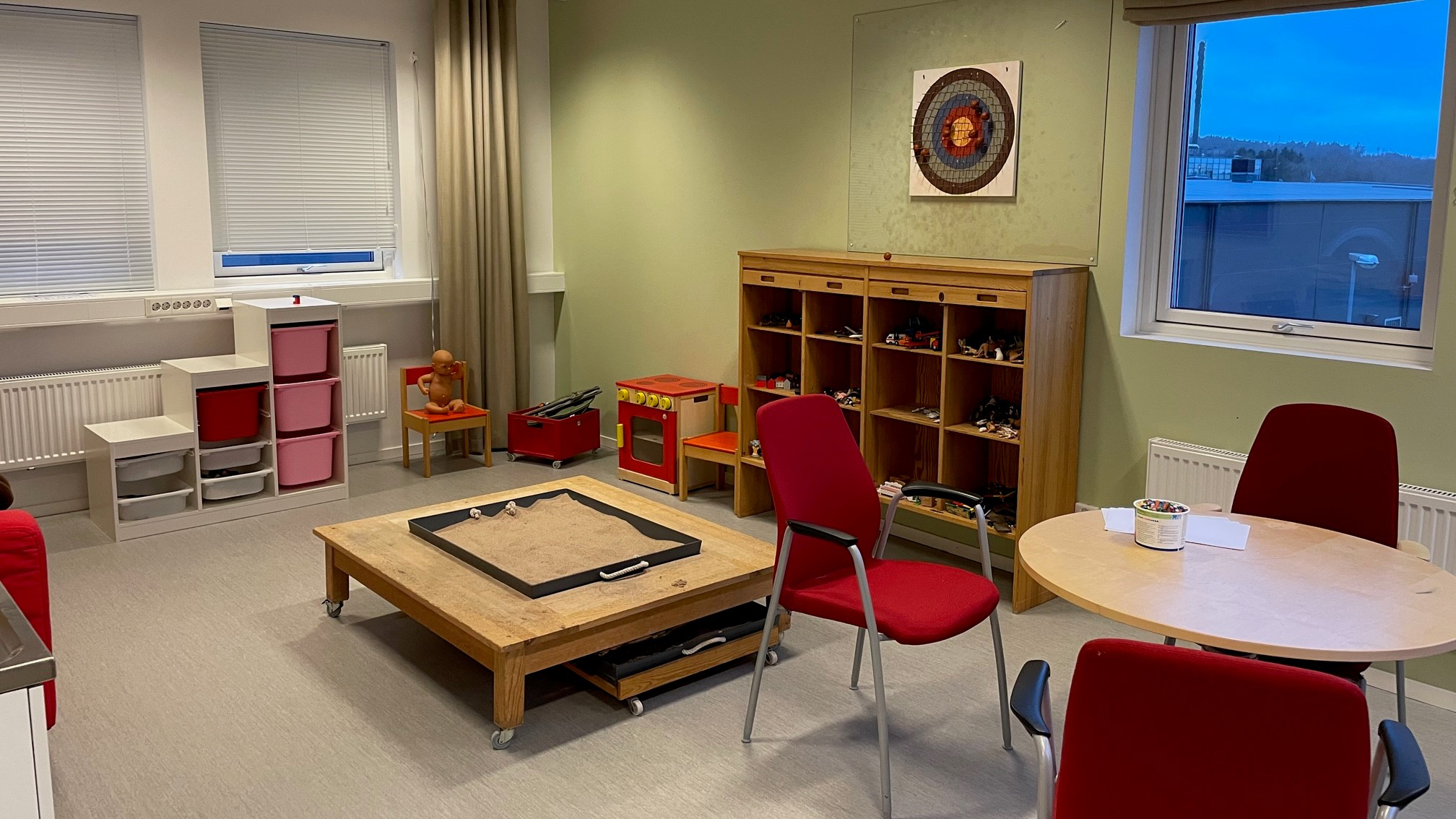 Rum med låga bord och hyllor, leksaksspis och leksaker i backar.