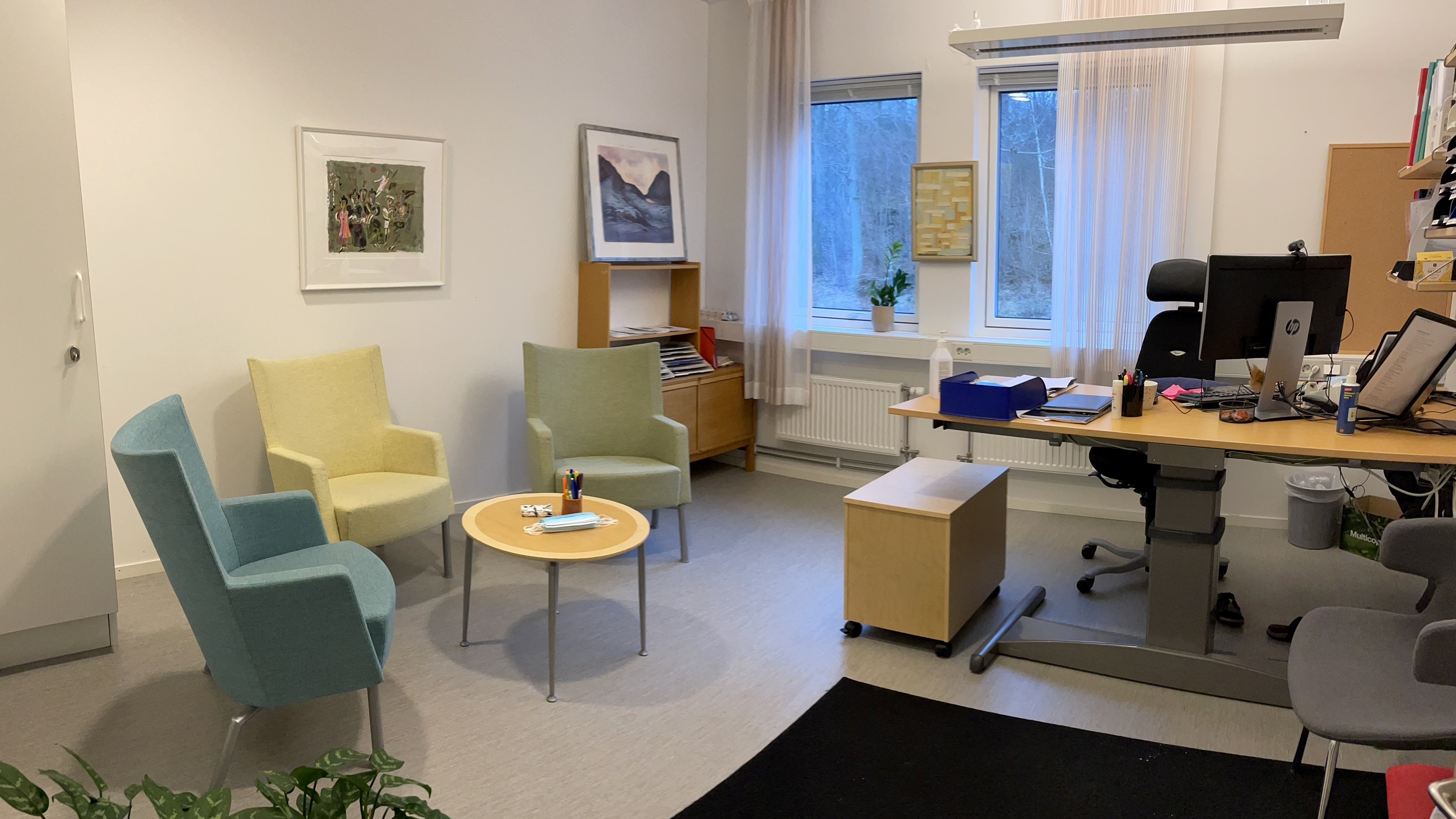 Mottagningsrum med fåtöljer samt skrivbord med dator och kontorsmaterial.