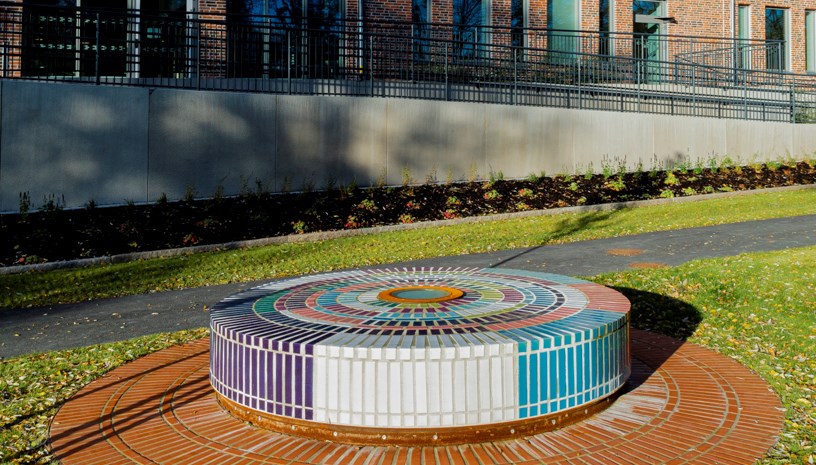 Rundel med färgade kakelplattor på en gräsmatta. I bakgrunden en röd tegelbyggnad.