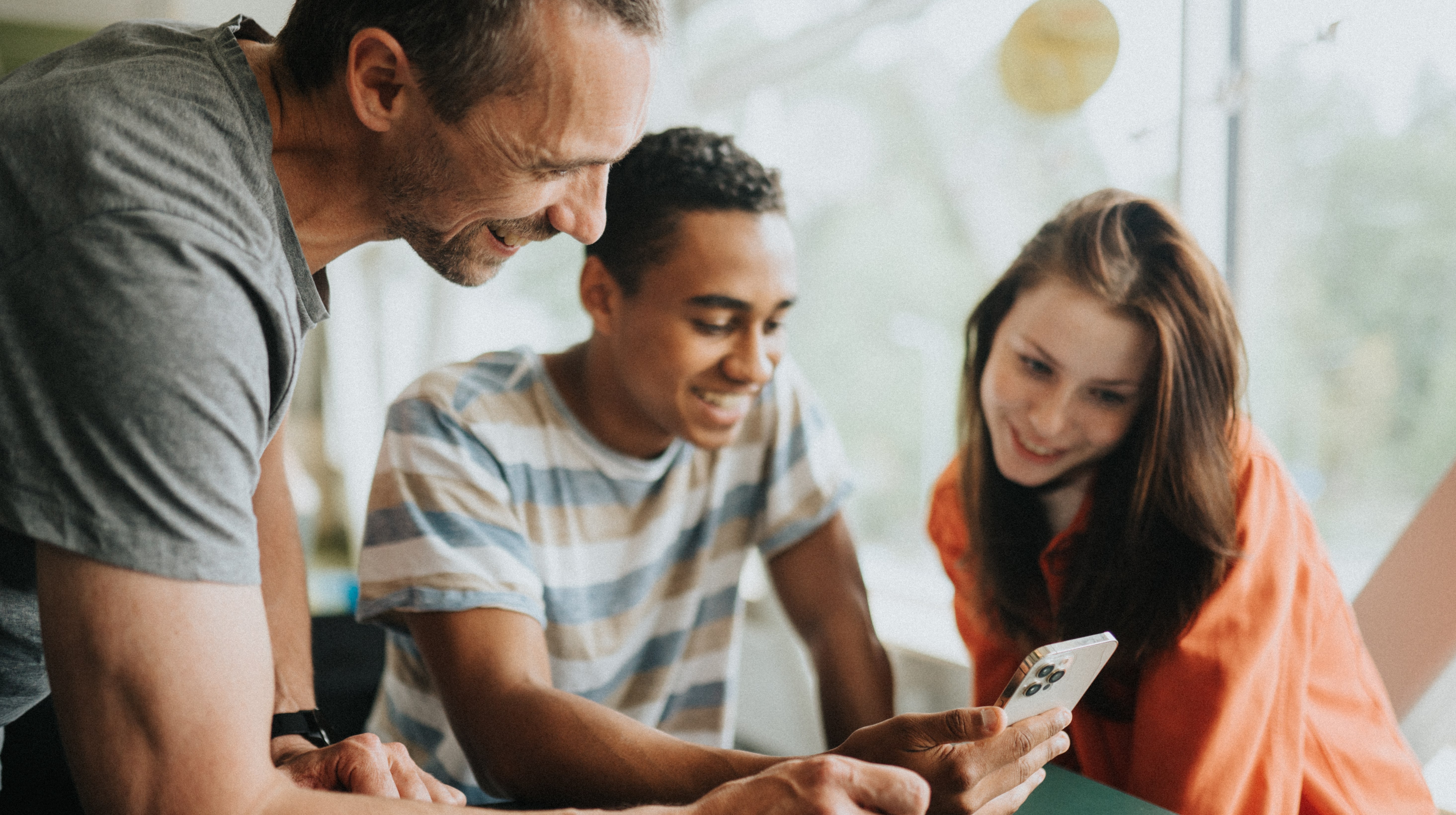 Två ungdomar sitter tillsammans med vuxen i skolmiljö eller på bibliotek